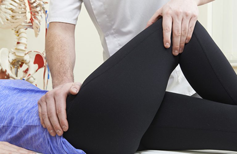 Male Osteopath Treating Female Patient With Hip Problem